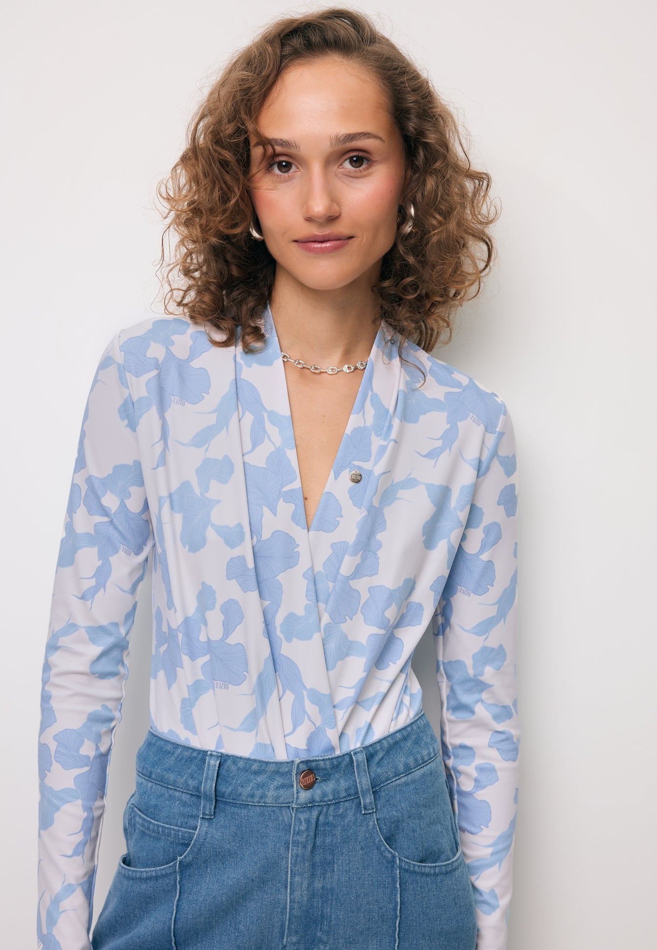 Modelka z rękoma w kieszeni spodni jeansowych BELINNA, ubrana w body w niebieski, kwiatowy print LOMMA.
