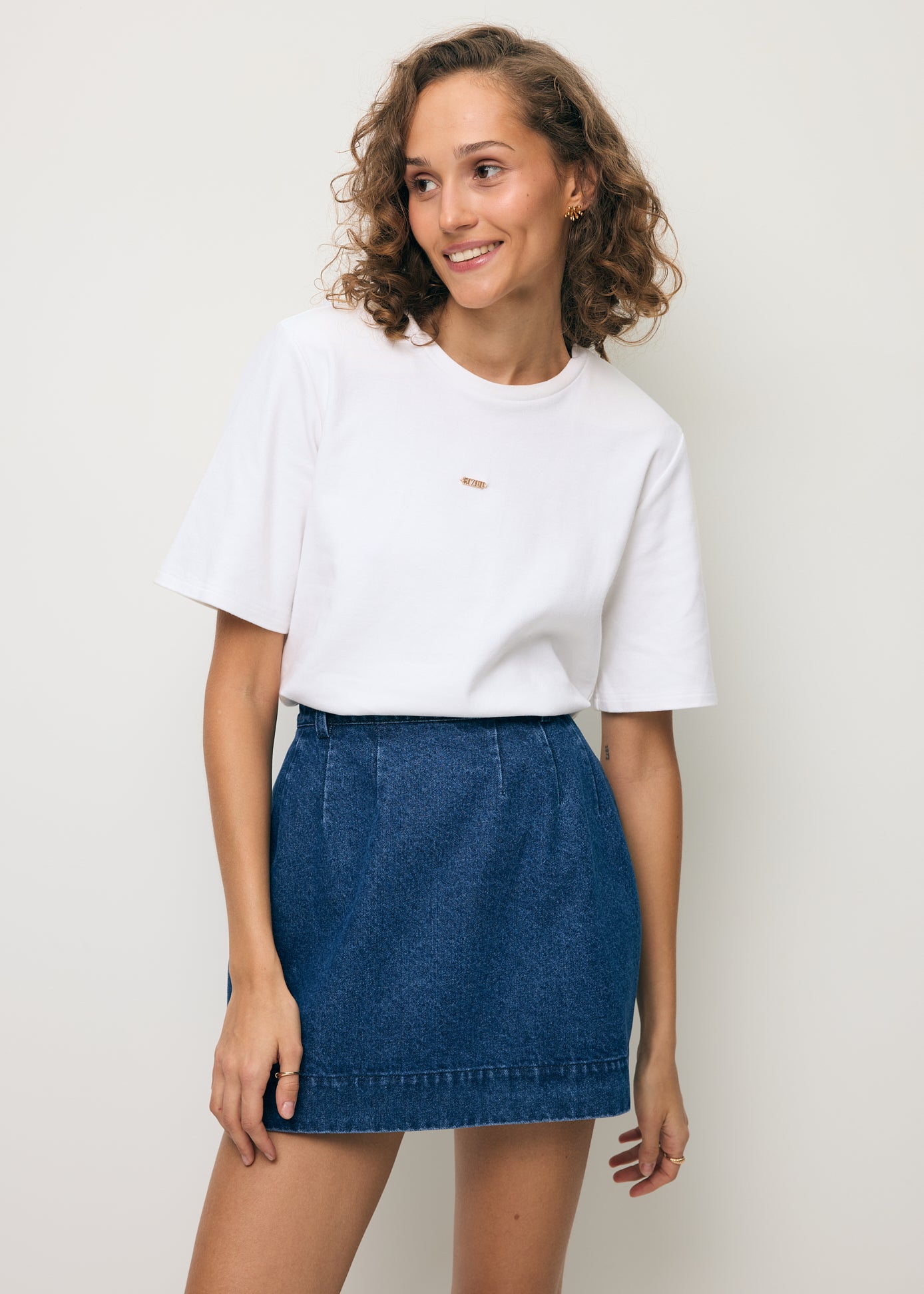 Modela ubrana w kremowy T-shirt MELISA z logo na przodzie oraz denimową spódniczkę BREDA.