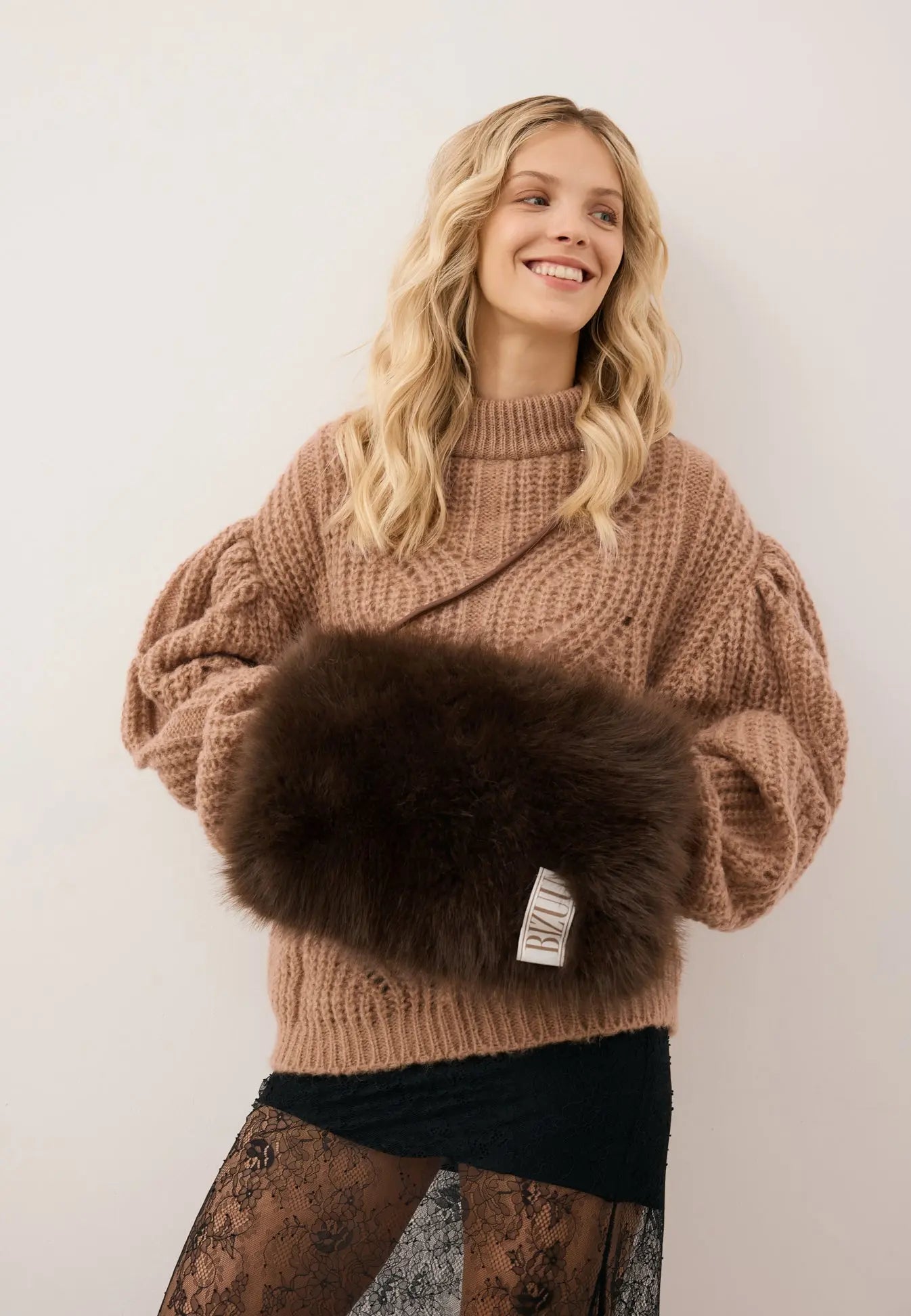 Uśmiechnięta modelka z rękoma w futrzanej muffce MUFFIE w kolorze brązowym.